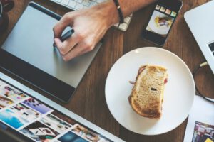 Draufsicht auf einen Frühstückstisch mit Sandwich und einem danebenliegenden Smartphone mit Benachrichtigungen als Symbol für fehlende Grenzen.