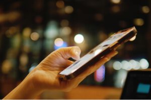 Nahaufnahme einer Hand, die im dunklen Umfeld auf einem Smartphone scrollt als Veranschaulichung der ständigen digitalen Interaktion.